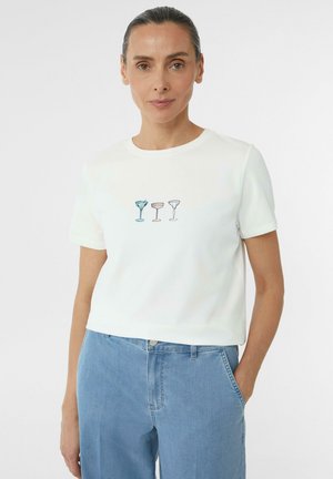T-shirt en coton blanc à manches courtes, avec des verres à cocktail brodés en bleu et couleurs pastel sur le devant. Coupe décontractée et col rond.