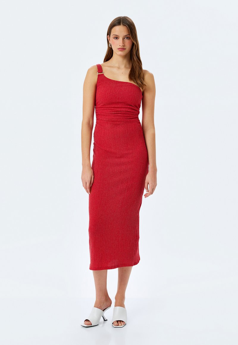 Robe midi rouge à rayures avec une bretelle et une boucle en argent décorative. Le tissu est texturé, ajusté et arrive au genou, assorti à des mules blanches.