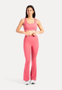 Roze sportoutfit bestaande uit een nauwsluitend crop top en een hoge taille flare legging, gemaakt van gladde, rekbare stof. Witte sneakers.