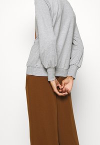 Grå sweatshirt med puffärmar, texturerad tyg och ribbad nederkant, i kombination med bruna vida byxor.