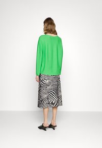 Pull vert en maille, jupe midi à rayures zébrées noir et blanc, et mules noires à talons. Texture douce, coupe décontractée et motifs uniques.
