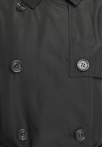 Černý dvouřadový trenčkot s velkými černými knoflíky, hladkou texturou a strukturovaným designem límce.