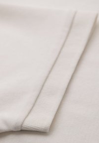 Bomull t-shirt i off-white med en mjuk textur, med en vikt ärm och en ribbad manschettdetalj.