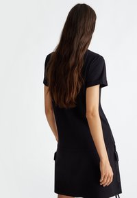 Abito nero realizzato in un tessuto morbido, maniche corte e vestibilità comoda. Presenta tasche laterali con dettagli in tessuto e orlo a lunghezza ginocchio.