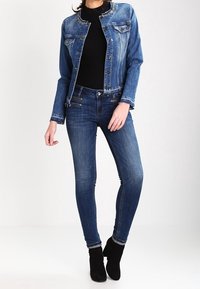 Džínová bunda s přiléhavým střihem, modrá barva a ozdobný výstřih. V kombinaci s tmavě modrými skinny džíny a černými kotníkovými botami.