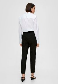 Camicia bianca a maniche lunghe, pantaloni neri a vita alta, silhouette elegante, vestibilità su misura, tessuto liscio e tacchi neri con cinturini.