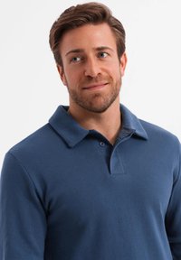 Polo en azul marino hecho de una tela texturizada que presenta un cuello, dos botones y un detalle de bolsillo en el pecho. El ajuste es relajado y casual.