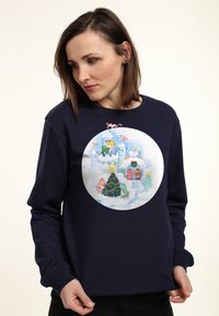 Tmavě modrý svetr se světle zabarvenou kulatou grafikou s hravými postavami kolem vánočního stromečku a hradu v scéně s mrakem.