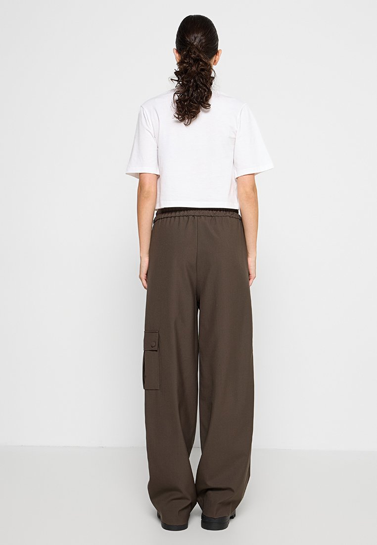 Braune weite Cargo-Hosen mit elastischem Bund, seitlichen Taschen und einer Knopftaschenklappe. Kombiniert mit einem schlichten weißen Cropped-T-Shirt.