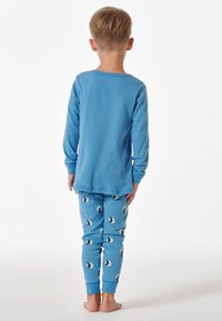 Haut à manches longues bleu associé à un pantalon de pyjama bleu avec un motif de lune croissante et de petits accents d'étoiles. Matière en coton doux.
