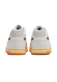 White leather sneakers with gray suede accents, orange rubber sole, mesh detailing, and padded collar. Rear view showcases distinct color blocks.
