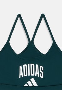Donkergroen sportbeha met dunne, verstelbare bandjes, voorzien van een groot wit "ADIDAS"-logo en een herkenbaar drie-strepen accent.