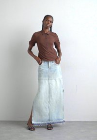 Bruine geribbelde polo met korte mouwen en kleine knopen, gecombineerd met een lichtblauwe denim maxi rok met een zijslit en een rafelige onderrand.