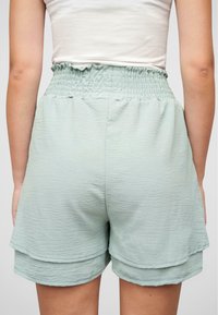 Lys grønne shorts med teksturert stoff, strikket midje og lagdelt design. Har en avslappet passform og sydd sømmer.