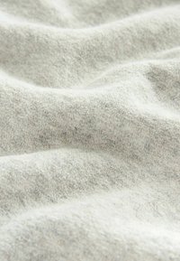 Hellgrauer Stoff mit einer weichen, strukturierten Oberfläche, die subtile Tonvariationen und ein leicht plüschiges Aussehen aufweist, und sanft in Falten gelegt.