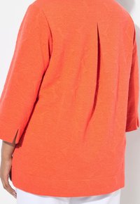 Jasně oranžový top s tříčtvrtečními rukávy, zdobený texturovaným vzorem listů a záhybem na zádech. Měkký, lehký materiál.