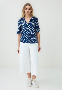 Blusa navy con motivo ondulato bianco, scollatura a V e maniche a palloncino corte, abbinata a culotte bianche e sneaker bianche.