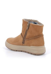 Stivali alla caviglia in suede marrone con zip laterale e fodera morbida. La suola è beige con una presa testurizzata, offrendo comfort e supporto.