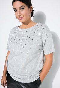 Szara krótki rękaw t-shirt z okrągłym dekoltem, ozdobiona przezroczystymi i czarnymi cyrkoniami. W połączeniu z czarnymi spodniami z ekoskóry.