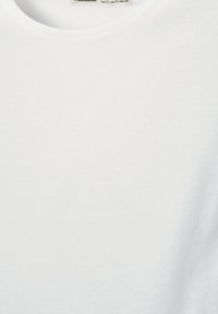 Bela bombažna majica z okrolim izrezom. Tkanina je gladka in lahka, brez vidnih vzorcev ali poudarkov. Oznaka je vidna na vrhu.