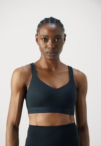 Svart sports-bh laget av elastisk materiale, med en v-halsdesign og et bredt, merkebånd for støtte. Glatt tekstur gjennom hele.