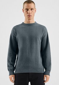 Ciemnoniebieski sweter dzianinowy z teksturowanym, ukośnym wzorem, okrągłym dekoltem oraz ściągaczami na rękawach i u dołu, pokazany na neutralnym tle.