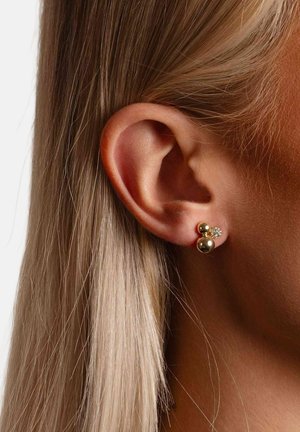 Gold-tone earrings with two spherical studs and a small crystal accent. Featured on an ear beside straight, light-colored hair.