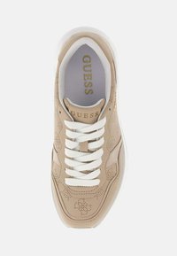 Sneaker beige con pelle perforata e lacci bianchi. Dotata di suola imbottita e logo "GUESS" in oro sulla linguetta. Design minimalista.