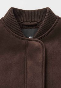 Giacca marrone con colletto a coste, tessuto morbido e design della chiusura pulito. Presenta un'etichetta interna nera.