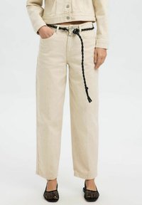 Beige wijde broek gemaakt van denim met een gevlochten zwarte riem, met zakken en een subtiele textuur. Gecombineerd met zwarte mesh schoenen.