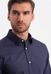 Camisa de color azul marino con botones, que presenta un sutil patrón geométrico, cuello clásico y botones blancos, elaborada en una tela suave.
