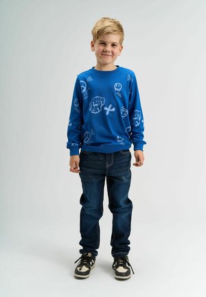 Blå bomulds sweatshirt med hvide grafiske prints, parret med mørke denim jeans og sorte sneakers med hvide detaljer.