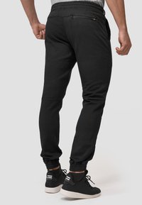 Pantalones joggers negros con cintura elástica, piernas ajustadas y puños en los tobillos; presenta un bolsillo con cremallera en la parte trasera.