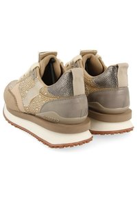 Sneakers da donna beige e in oro metallico con tessuto testurizzato, suole bianche spesse, battistrada marrone e linguette sul tallone.