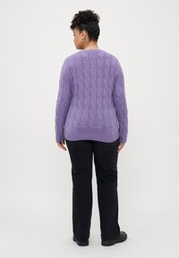 Lila Strickpullover mit langen Ärmeln, geripptem Saum und strukturiertem Muster. Kombiniert mit schwarzen Hosen und flachen Schuhen.