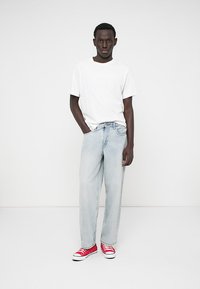 T-shirt en coton blanc, jeans en denim baggy bleu clair, baskets basses rouges. Design simple, sans motifs visibles, arrière-plan neutre.