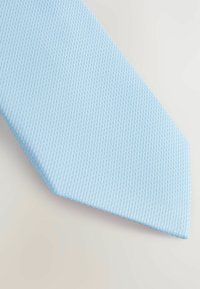 Cravate bleu clair avec une texture à motif côtelé, présentant une extrémité pointue et un tissu lisse.