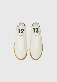 Zapatillas blancas con acabado texturizado, que cuentan con una suela de goma, acentos en el talón en negro y números impresos "1973" en negrita negra.