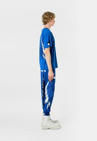 Camiseta de algodón azul con diseño de alas en la parte de atrás, combinada con pantalones de chándal azul a juego que presentan acentos de alas, y botas gruesas blancas.