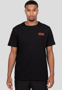 Sort bomulds-t-shirt med en rød broderet "WRONG FRIENDS" logo på venstre bryst. Klassisk rund hals og korte ærmer.