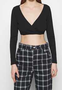 Top corto nero a costine con scollo a V profondo e maniche lunghe, abbinato a pantaloni a quadri a vita alta blu navy e bianchi.