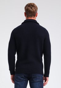 Pull en tricot bleu marine avec un col haut et une texture côtelée, doté de manches longues et d'un ourlet ajusté. Vue de dos montrant les coutures des épaules.