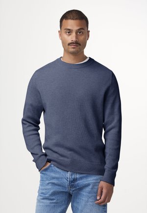 Navy ribbed sweater with a round neckline and long sleeves, paired with light blue denim jeans. Smooth fabric texture, casual design.