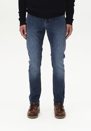 Blaue Jeans aus Denim im Slim-Fit mit ausgewaschenen Details. Kombiniert mit braunen Lederboots und einem dunklen Pullover.
