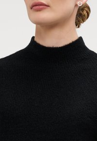 Maglione nero a maglia con colletto alto, caratterizzato da un motivo testurizzato. Vista ravvicinata che mette a fuoco il collo e la parte superiore del torso.