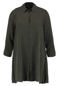 Camicia nera con bottoni, a pois bianchi, maniche lunghe e colletto; realizzata in tessuto morbido con una vestibilità leggermente ampia e fessure laterali.