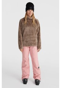 Bruine fleece pullover met hoge kraag, in combinatie met roze waterdichte sneeuwbroek en zwarte skibotten. Zwarte beanie met logo-detail.