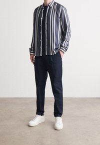 Randig skjorta i marinblått och vitt, långärmad, ihop med mörka byxor och vita sneakers; slät tyg med en klassisk design.