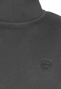 Maglione a collo alto in maglia a righe grigio scuro con un piccolo logo ricamato a forma di scudo sul petto.
