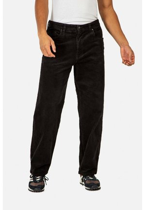 Schwarze Cordhosen mit geradem Bein, ausgestattet mit frontalen Taschen und einer strukturierten Oberfläche. Kombiniert mit schwarzen Sportschuhen.